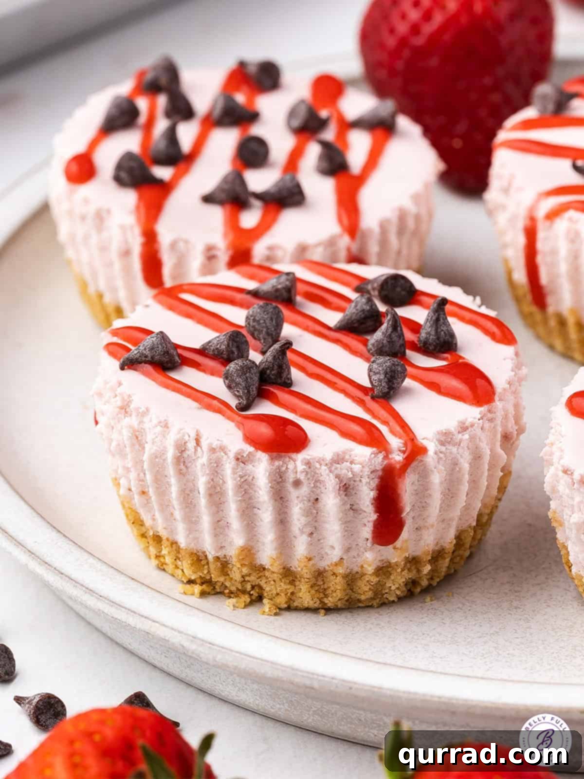 These No Bake Mini Strawberry Cheesecakes are sweet, tart, and irresistible. The filling is smooth, creamy and light, thanks to the Cool Whip. Mini strawberry cheesecakes on a plate, garnished with fresh strawberries