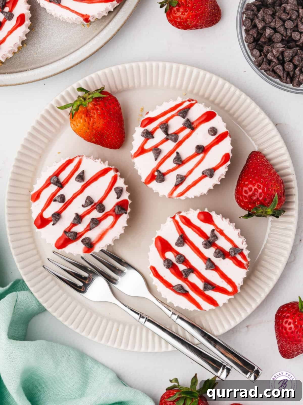 These No Bake Mini Strawberry Cheesecakes are sweet, tart, and irresistible. The filling is smooth, creamy and light, thanks to the Cool Whip. Overhead view of miniature strawberry cheesecakes artfully arranged on a plate, showcasing their vibrant color and perfect size.