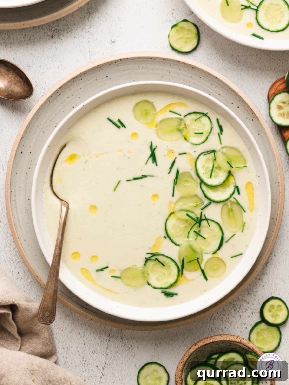 Overhead view of a bowl of cold cucumber soup, garnished with fresh herbs and a swirl of olive oil, ready to be served on a hot summer day.