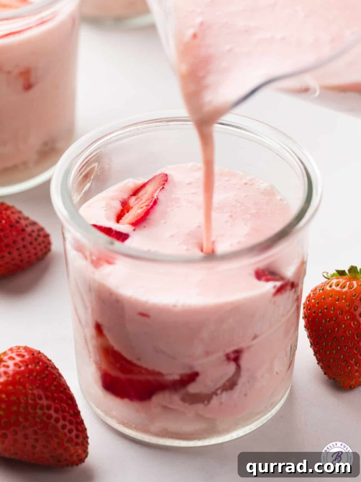 Pouring Fresh Strawberries and Cream Agua Fresca Over Ice Creamy strawberry agua fresca being poured from a pitcher into a tall glass filled with ice, illustrating its refreshing appeal.