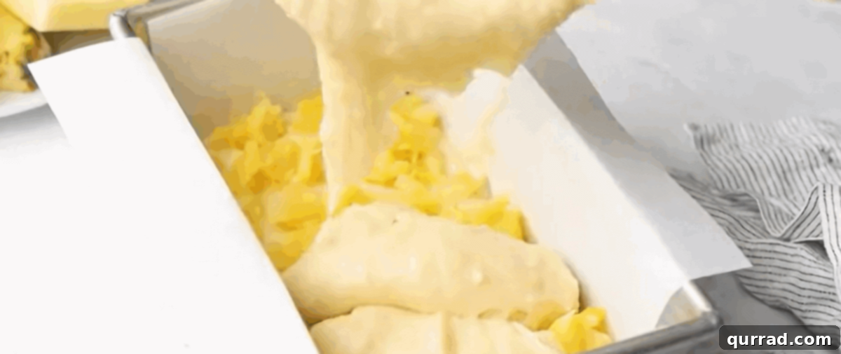A partially filled parchment-lined loaf pan showing the first layer of golden batter topped with a scattering of glistening crushed pineapple, ready for the next layer.
