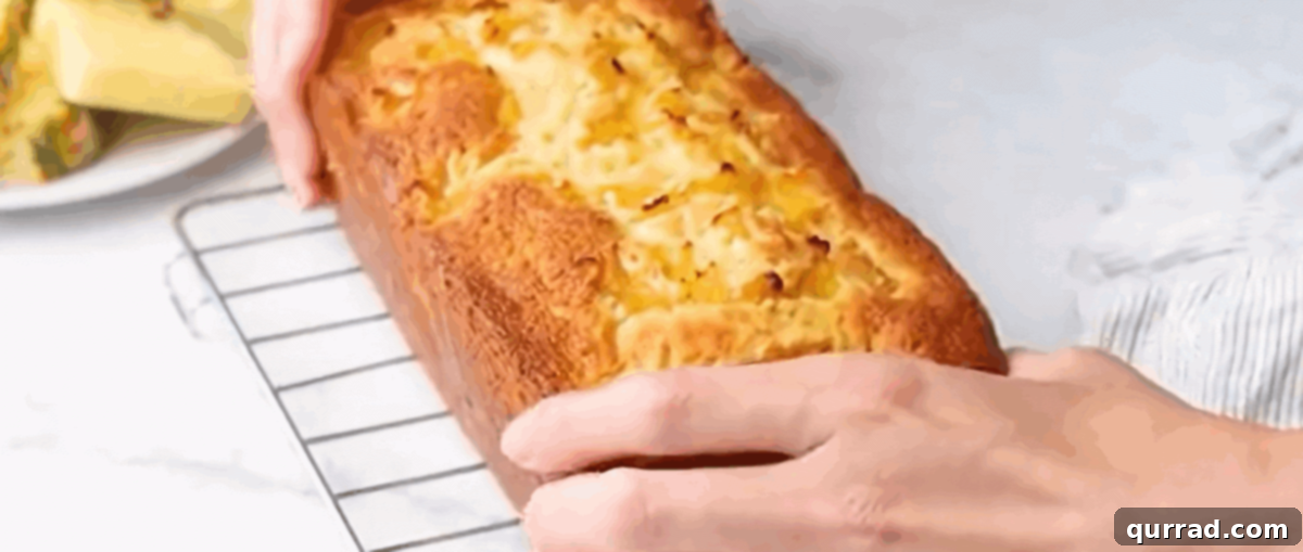 A freshly baked, golden-brown pineapple bread loaf resting on a metal cooling rack, steam gently rising, indicating its warmth and readiness for glazing.