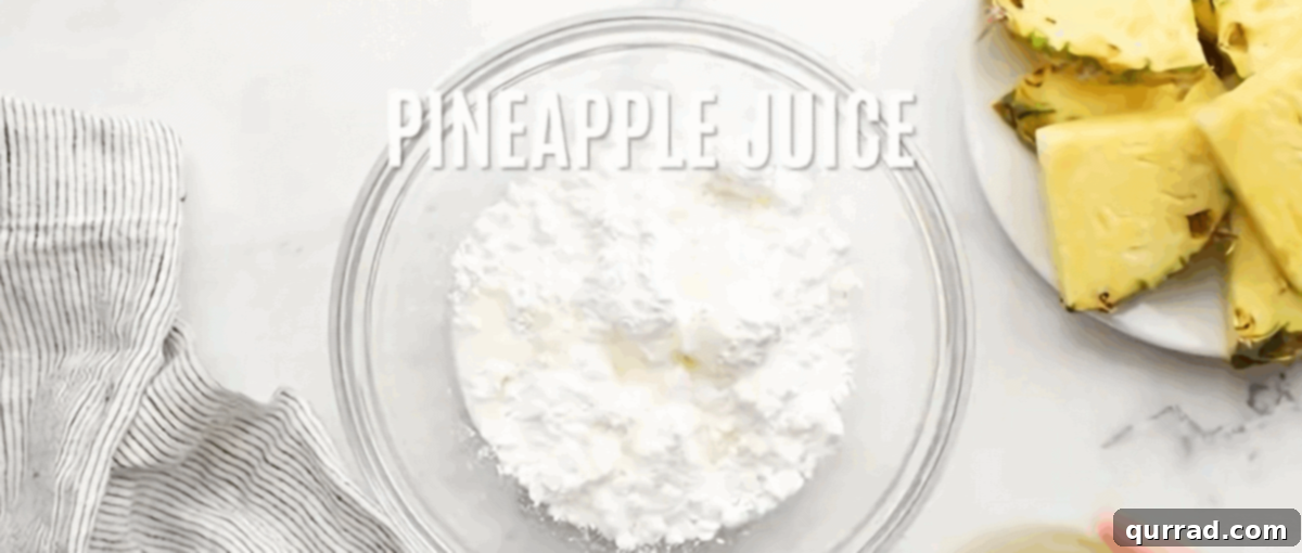 A whisk vigorously blending powdered sugar, milk, and pineapple juice in a clear glass bowl, creating a smooth, luscious glaze for the pineapple bread.