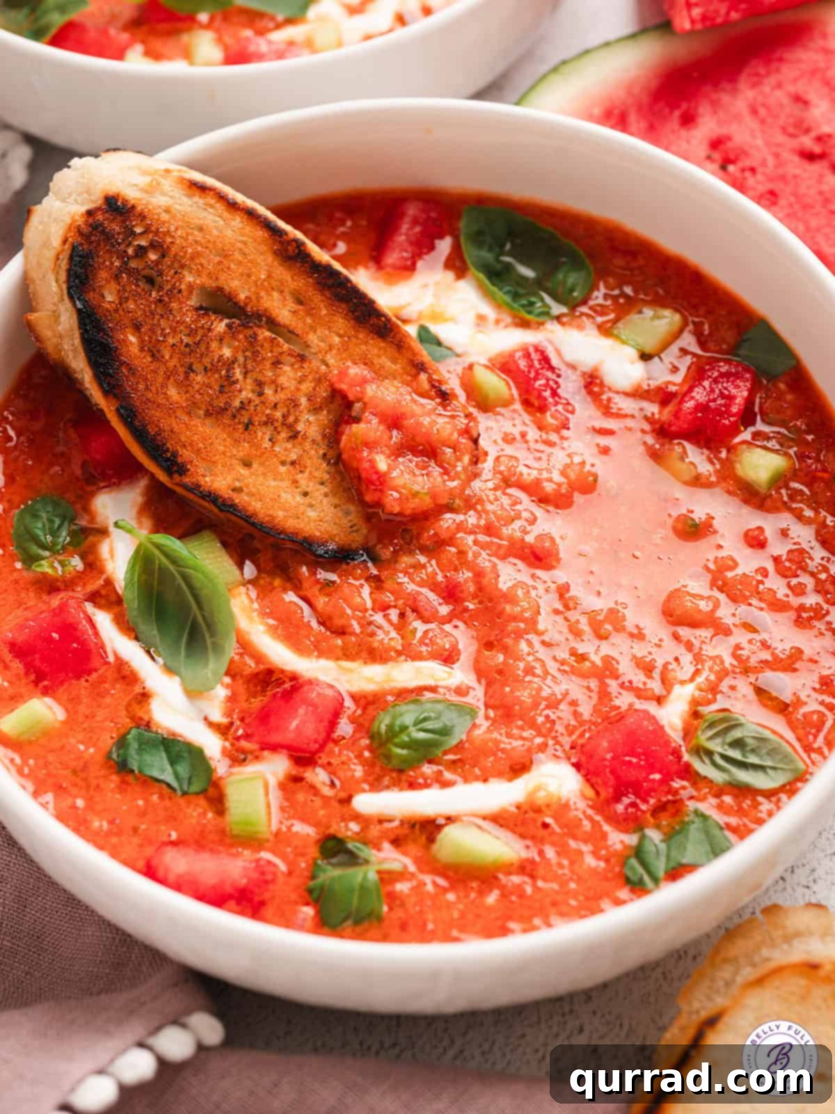 A beautiful bowl of watermelon gazpacho, garnished with fresh basil and a drizzle of olive oil, served alongside crusty bread.