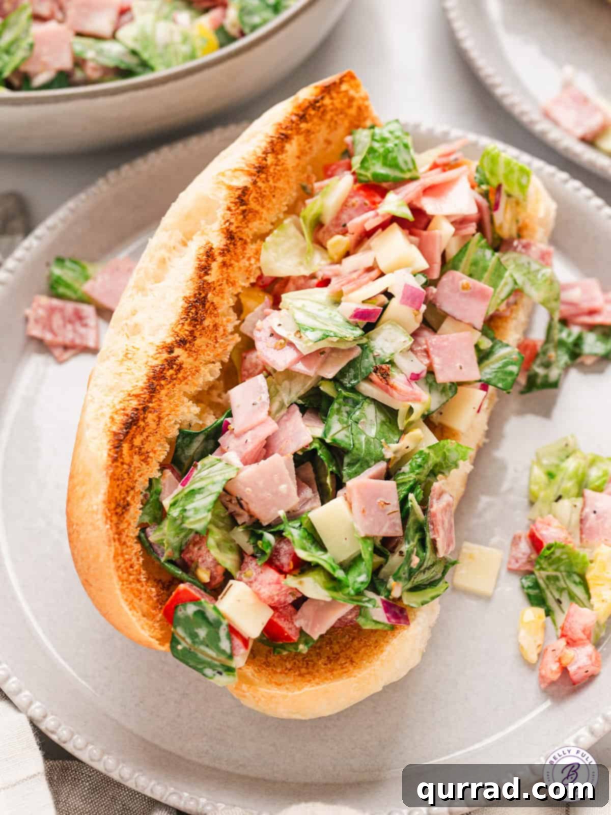 A delicious Chopped Italian Sandwich featuring lettuce, salami, ham, and provolone, all tossed with a zesty mayo, oil, and vinegar dressing, piled high on a hoagie bun. A vibrant, overflowing Chopped Italian Sandwich with lettuce, meats, and cheese on a plate, ready to be enjoyed.