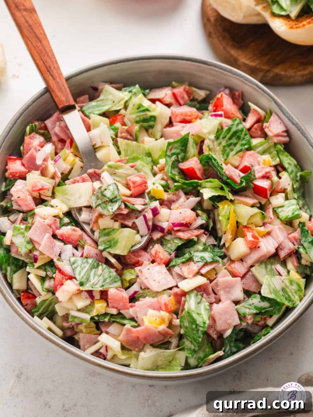 The vibrant and fresh mix of lettuce, salami, ham, and provolone, tossed with a tangy dressing, ready for your Chopped Italian Sandwich. A bowl filled with finely chopped Italian salad ingredients, before being placed into hoagie buns.