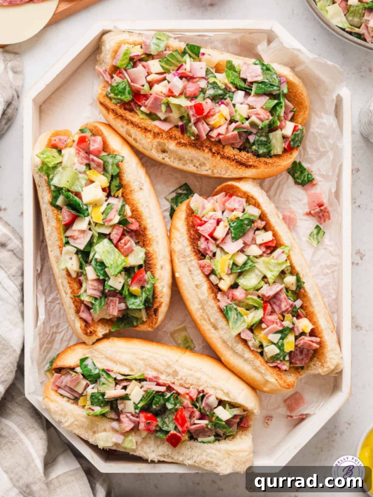 A platter of Chopped Italian Sandwiches, featuring lettuce, salami, ham, and provolone tossed with a mayo, oil, and vinegar dressing, piled high on hoagie buns. An overhead view of four perfectly assembled chopped Italian sandwiches on a serving tray, ready to be enjoyed.
