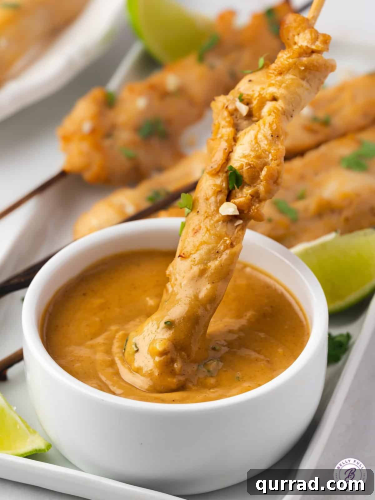 Grilled chicken skewers being dipped into a rich peanut sauce.