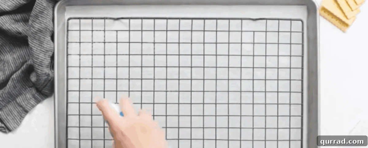 A hand spraying a wire rack with non-stick cooking spray, placed over parchment paper on a baking sheet.