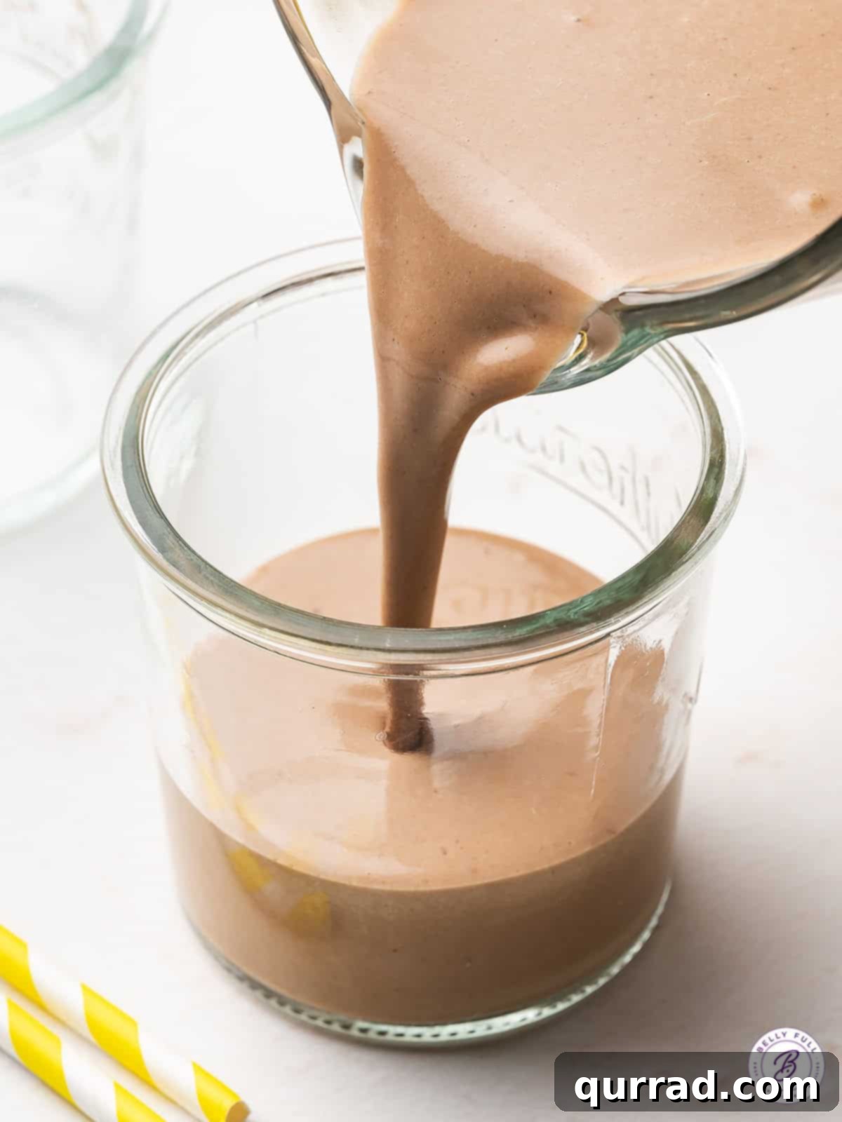 Close-up shot of a thick, creamy chocolate banana smoothie being poured into a tall glass from a blender.