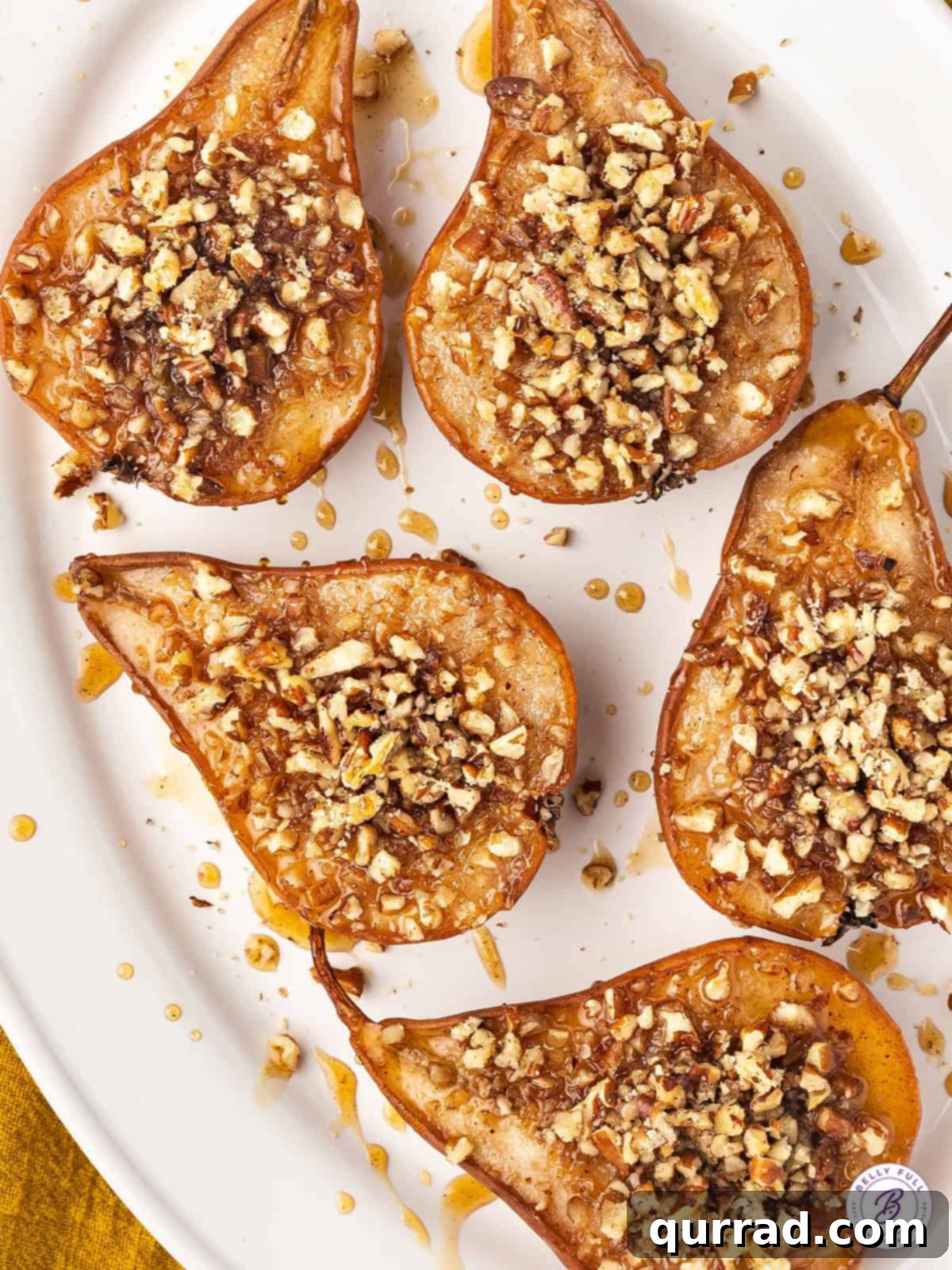 Perfectly spiced and sweetened with honey, this Baked Pears recipe requires just 5 ingredients. Serve with a scoop of vanilla ice cream. A white plate featuring two halves of baked pears, generously topped with a medley of chopped nuts and a sweet drizzle, highlighting their rustic charm and delectable warmth.