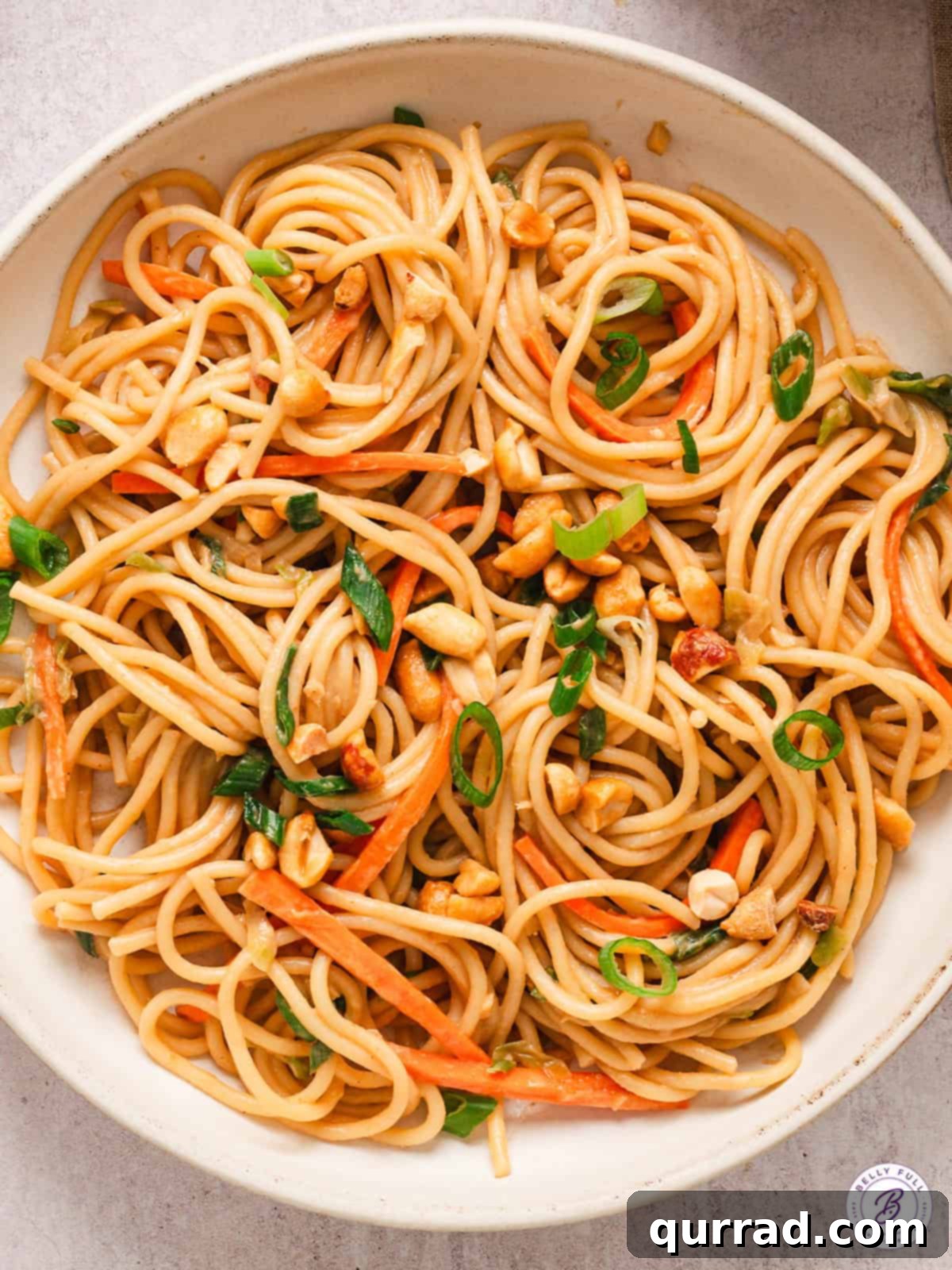 A white bowl of peanut noodles, garnished with fresh herbs and crushed peanuts