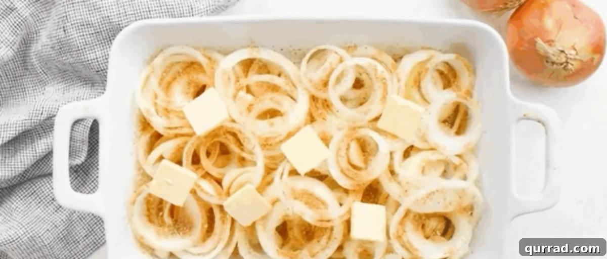 Pats of butter strategically placed on top of the seasoned onion rings in a white casserole dish.