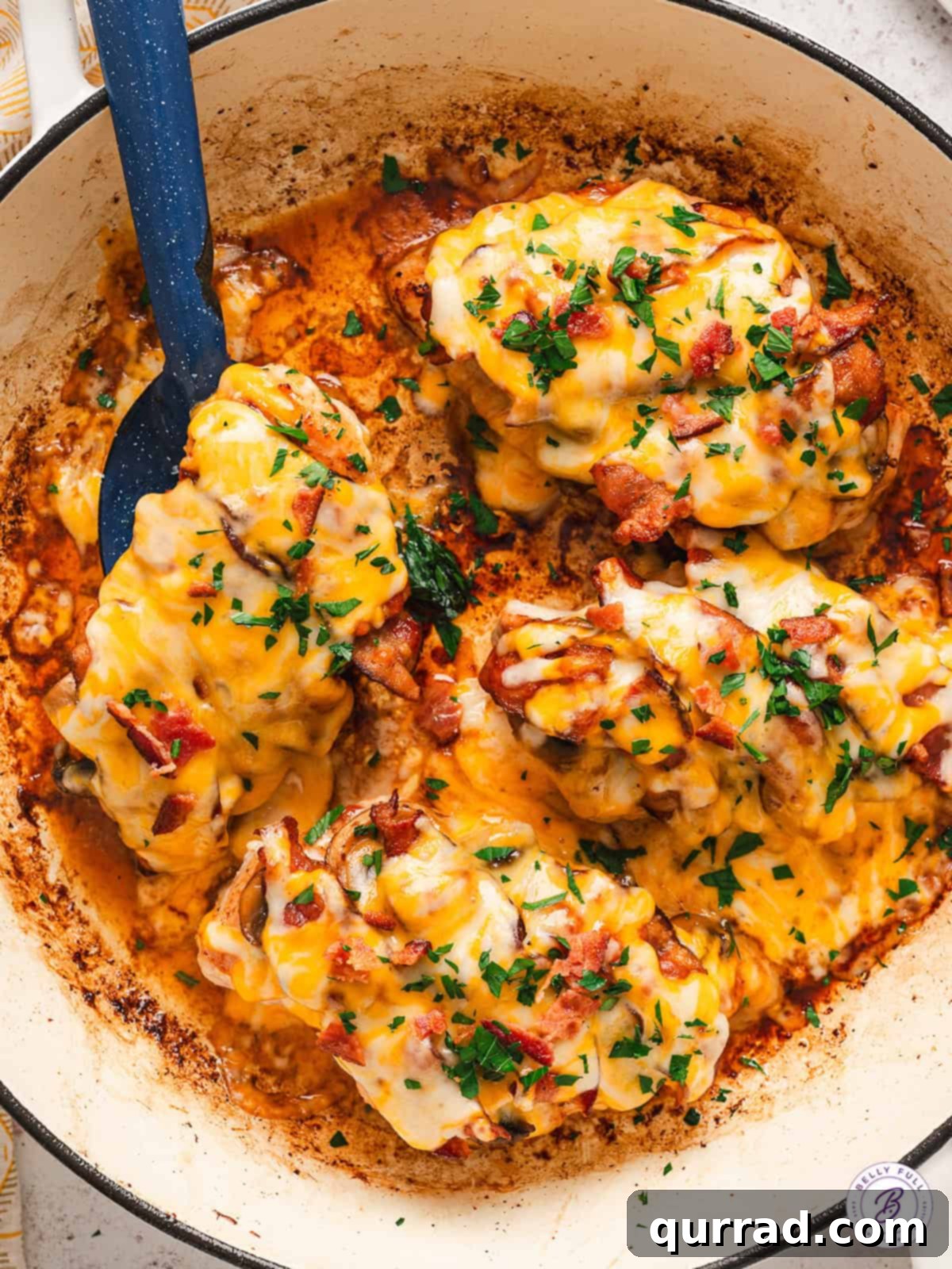 Alice Springs Chicken features juicy chicken breasts topped with a creamy honey mustard sauce, mushrooms, crispy bacon, and cheese. Overhead view of a skillet of Alice Springs chicken with a spatula under one chicken breast.