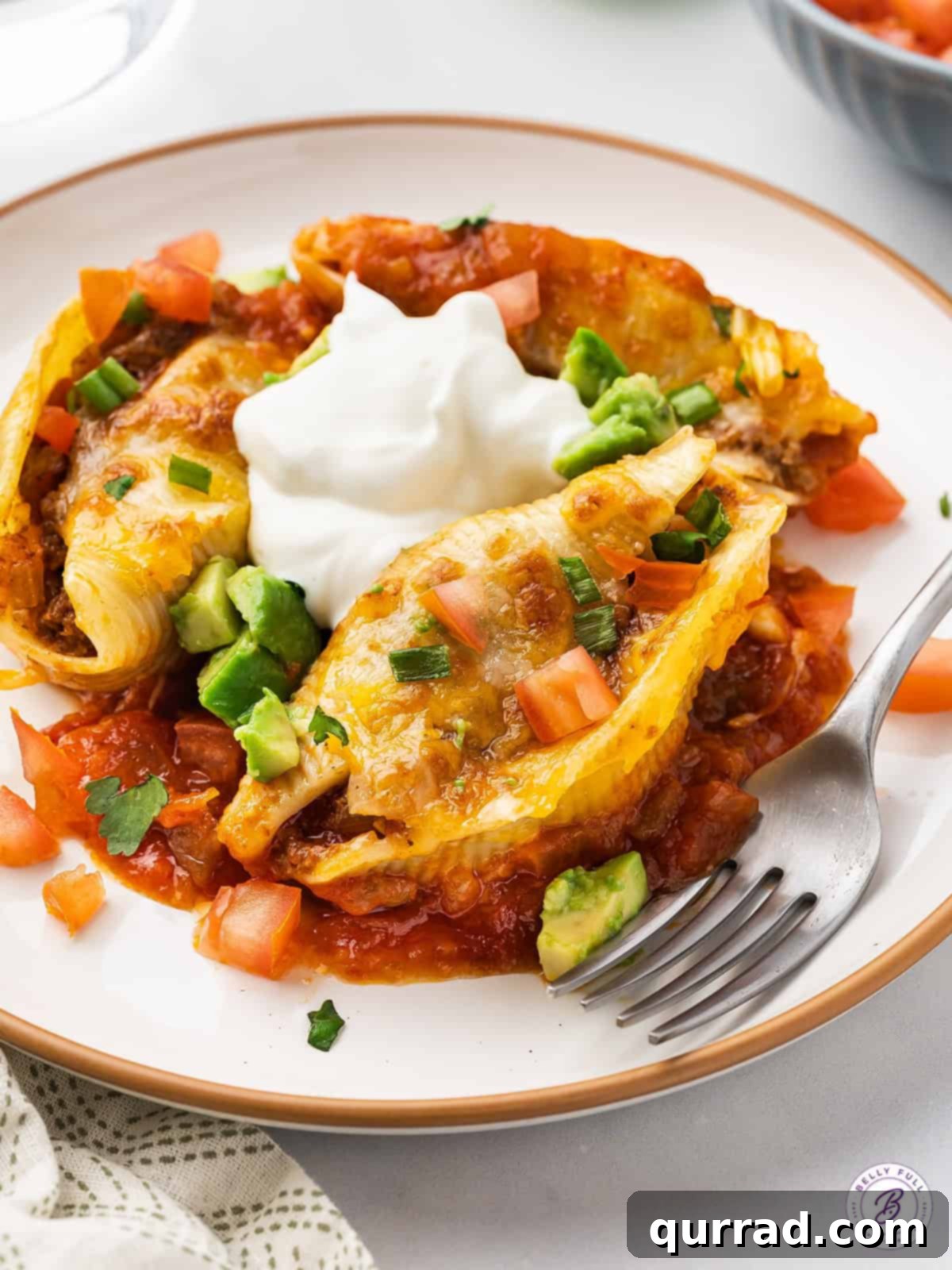 Jumbo pasta shells are stuffed with a mixture of taco meat, diced tomatoes, and cheese in this easy Taco Stuffed Shells recipe. A close-up of cheesy taco stuffed shells in a baking dish, with a serving spoon.