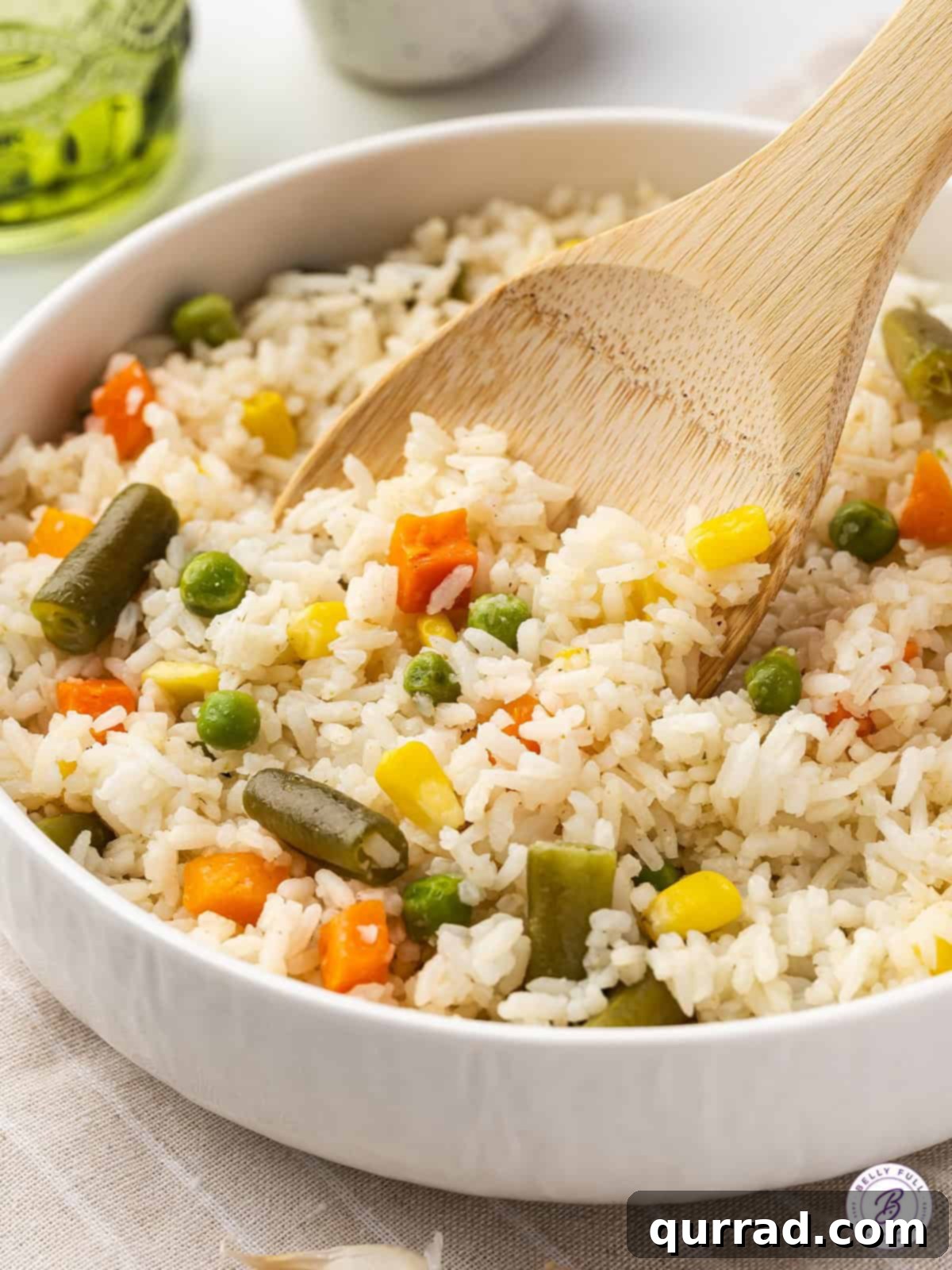 Fluffy white rice and frozen veggies are lightly seasoned and buttered in this Mixed Veggies and Rice recipe. A wooden spoon stirring a bowl of fluffy mixed vegetables and rice, highlighting its vibrant colors and comforting texture.