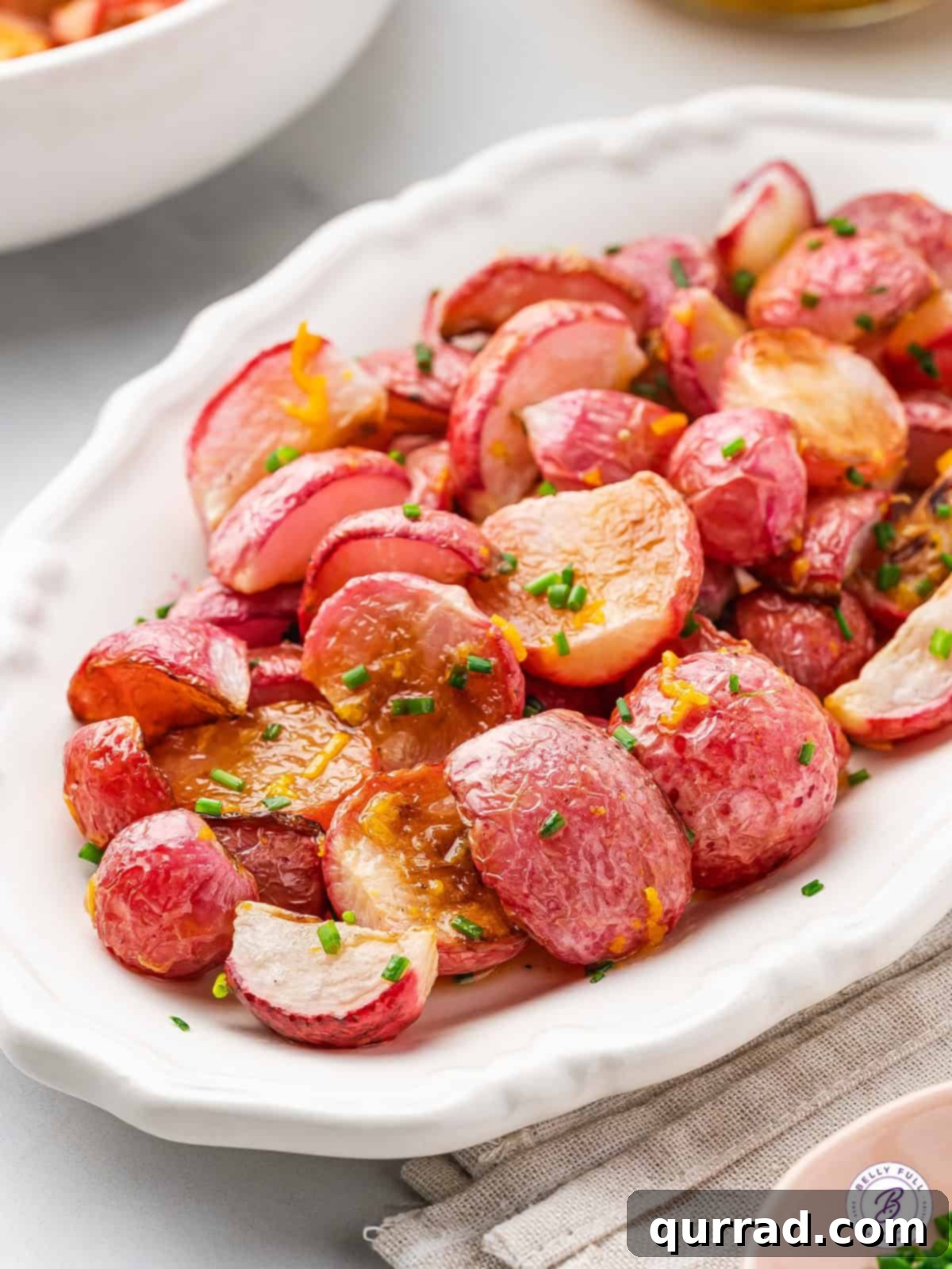 Roasted radishes on a white platter, garnished with fresh chives, ready to serve.