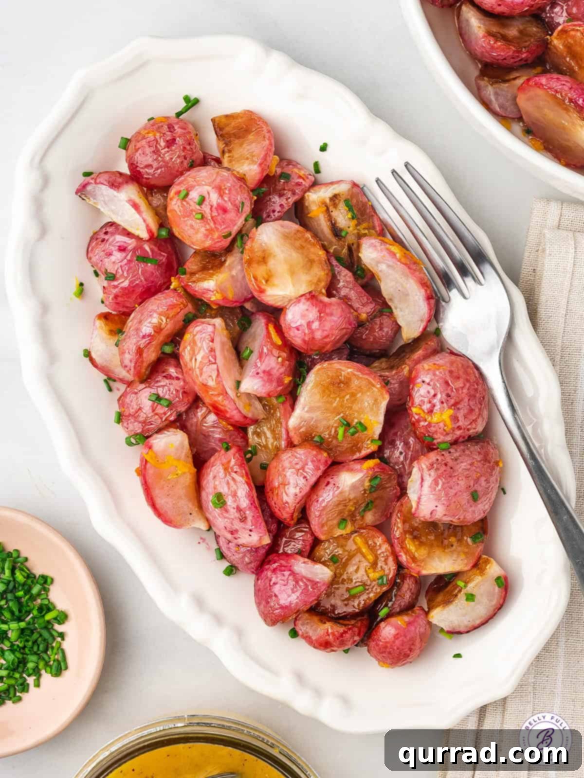 Overhead view of a platter of oven roasted radishes, garnished with fresh herbs.
