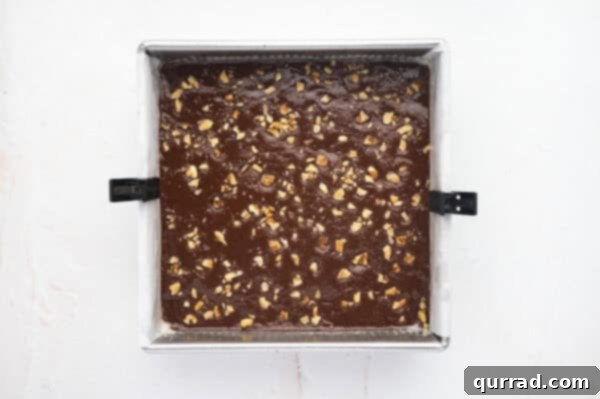 Fudge mixture in a parchment-lined baking dish topped with chopped walnuts.