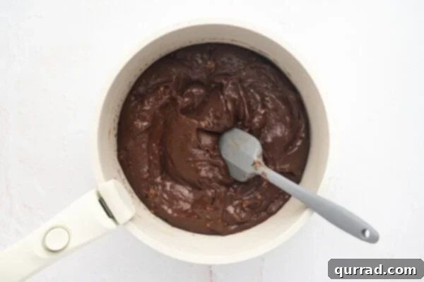 Fudge base mixture in a saucepan being stirred with a spatula, showing the melting process.