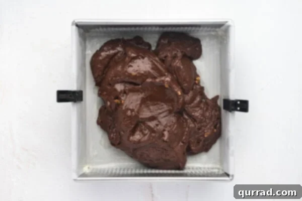 Chocolate fudge mixture being spooned into a parchment-lined baking dish.