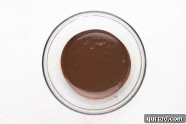 Smooth, melted chocolate in a clear glass mixing bowl, cooled and ready for the next step.