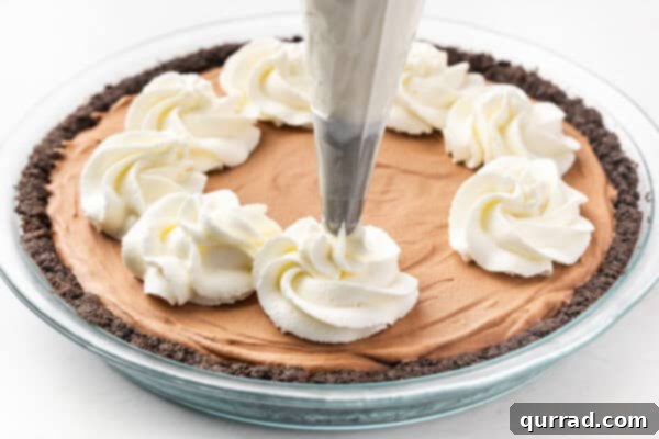 A piping bag meticulously adding swirls of homemade whipped cream onto a French silk pie.