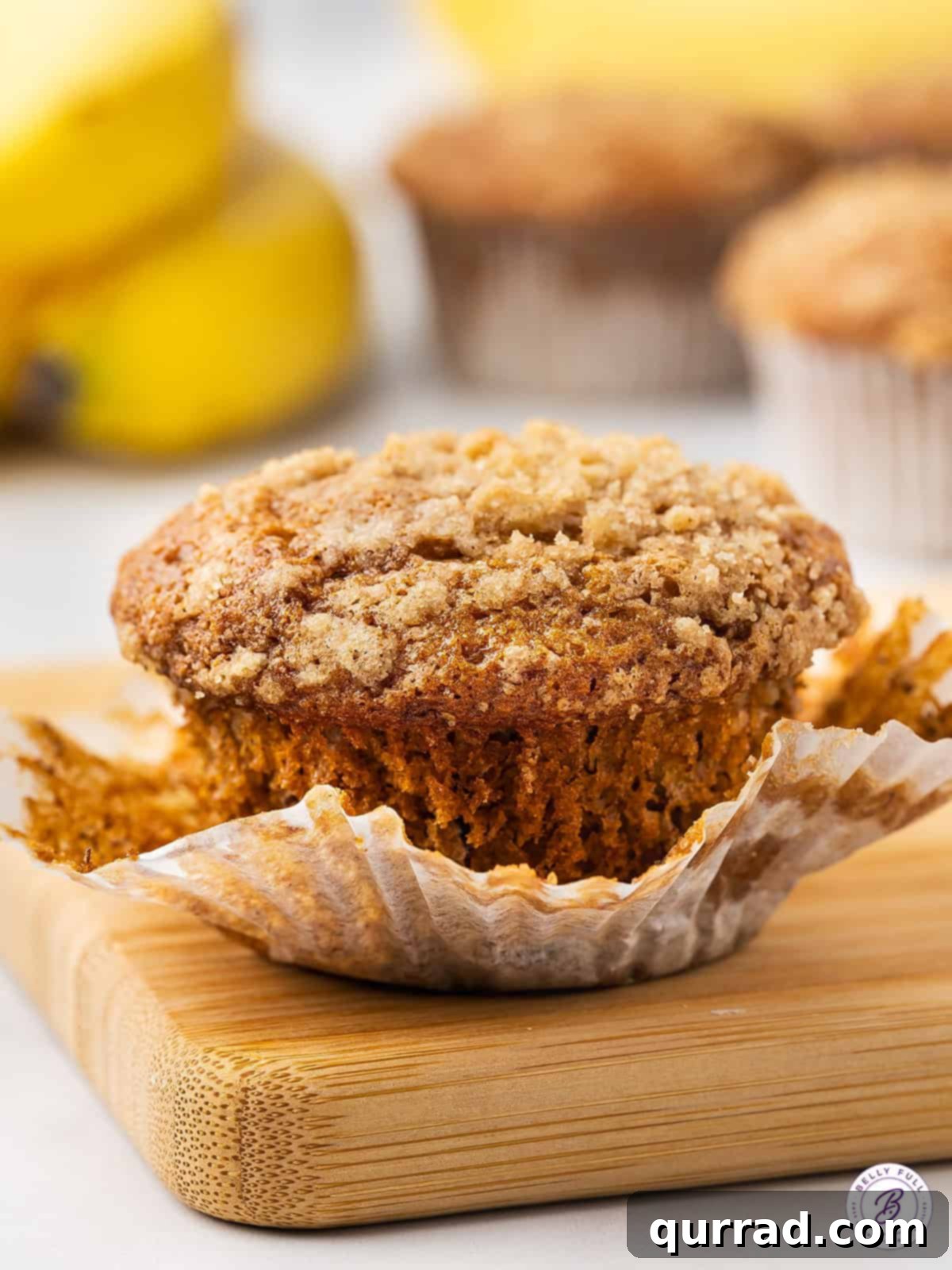 A single banana crumb muffin with the paper wrapper peeled down, showcasing its moist interior