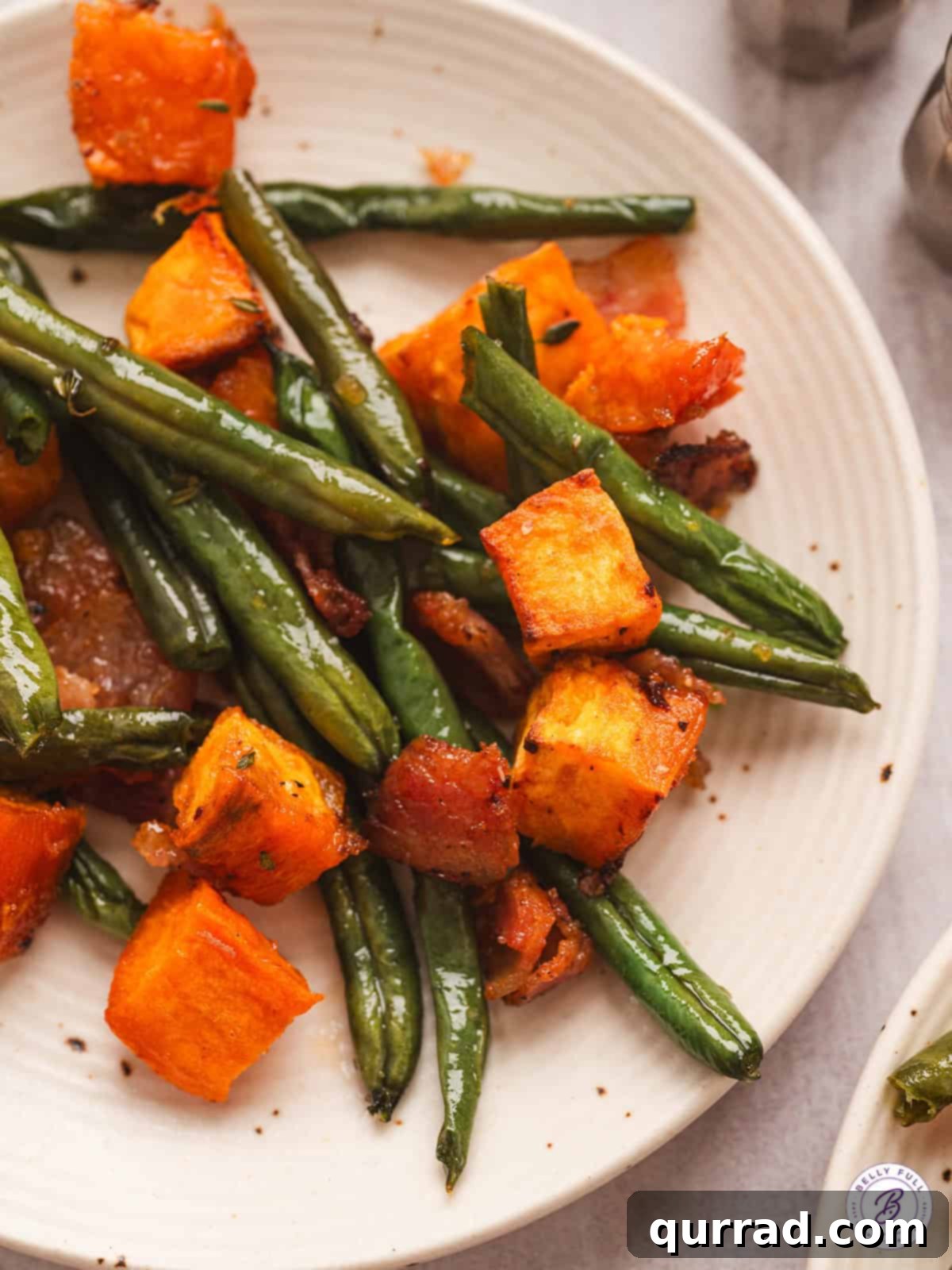 A plate of perfectly roasted Sheet Pan Sweet Potato Supper – a delightful combination of sweet potatoes, green beans, and crispy bacon. Roasted sweet potatoes and green beans with bacon served on a white plate, ready to eat.