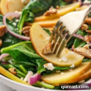 A fork in an apple slice in a spinach apple salad, emphasizing the fresh ingredients.