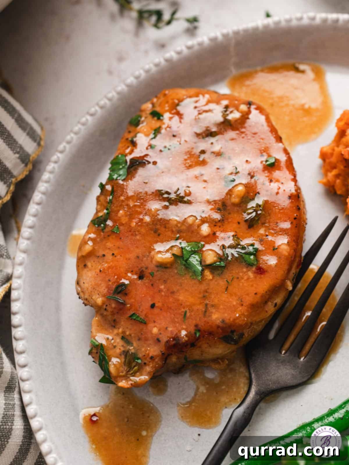 An apple cider glazed pork chop served on a pristine white plate