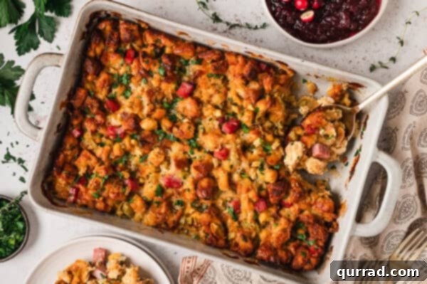Baked ham and gruyere stuffing in a casserole dish with a serving spoon, ready to be enjoyed