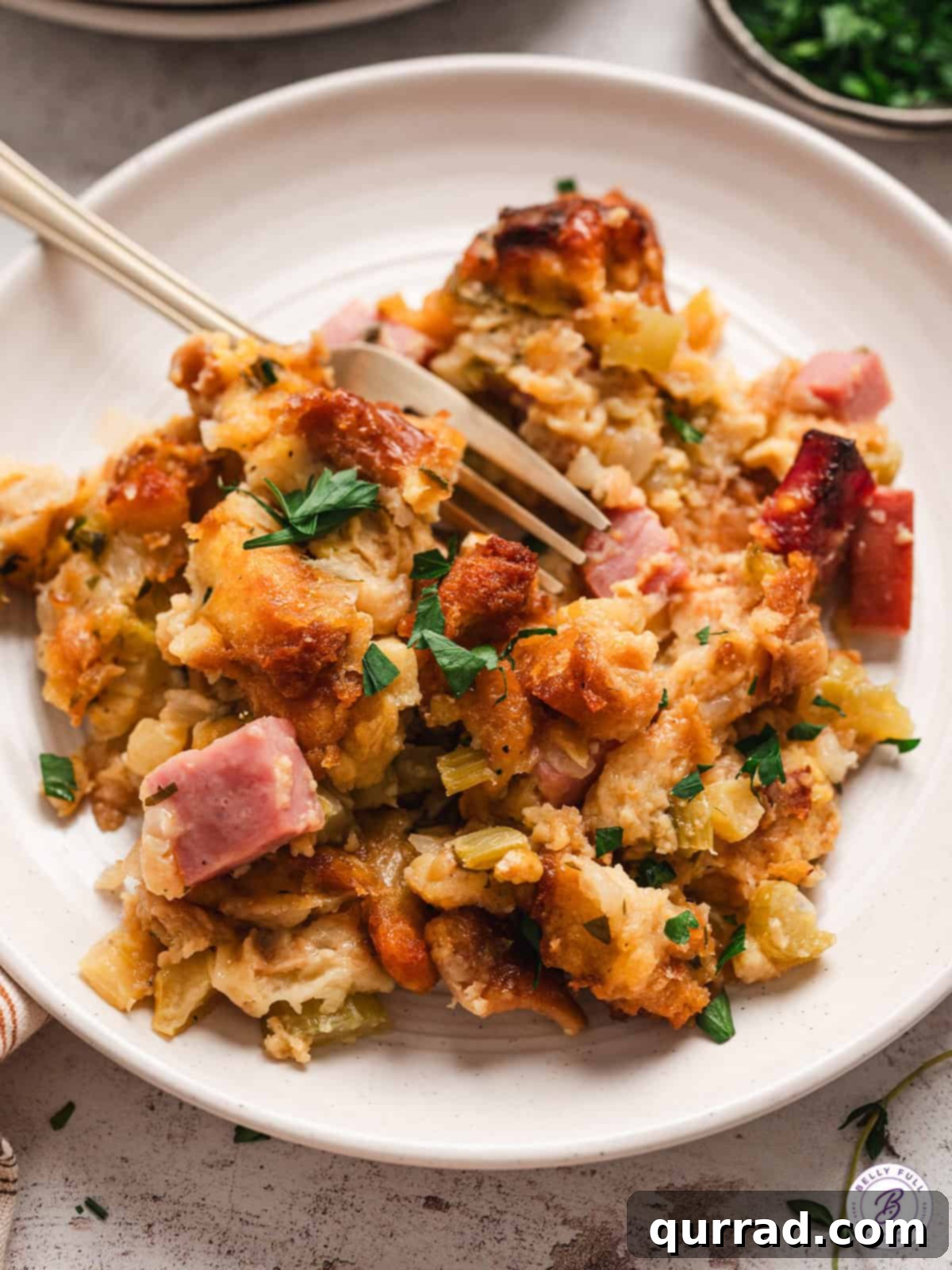 A plate of golden, baked potato bread stuffing with visible ham and apple pieces