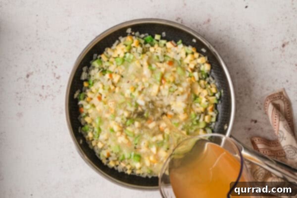 Pouring broth into a skillet with softened celery, onions, and apples, creating the stuffing base