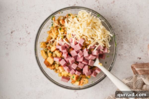 Cubes of bread, shredded cheese, and diced ham in a mixing bowl, ready for baking
