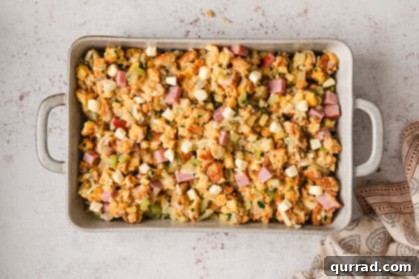 Unbaked ham and gruyere stuffing mixture spread on a pan, topped with butter cubes