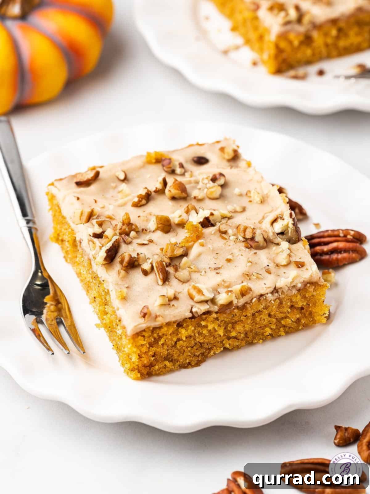 A perfectly sliced piece of pumpkin sheet cake on a white plate, showcasing its moist texture and creamy cinnamon frosting, ready to be enjoyed.