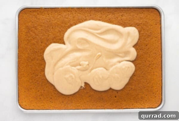 Smooth cinnamon frosting being spread over a pumpkin sheet cake