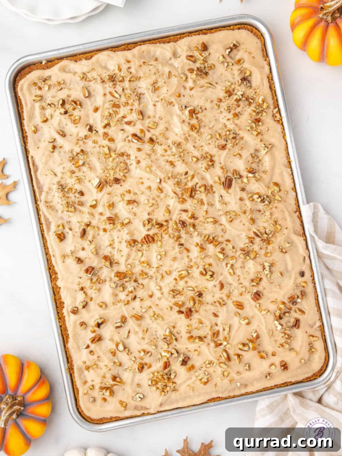 A freshly baked pumpkin sheet cake, still in its baking pan, generously topped with a smooth, glistening layer of cinnamon frosting.