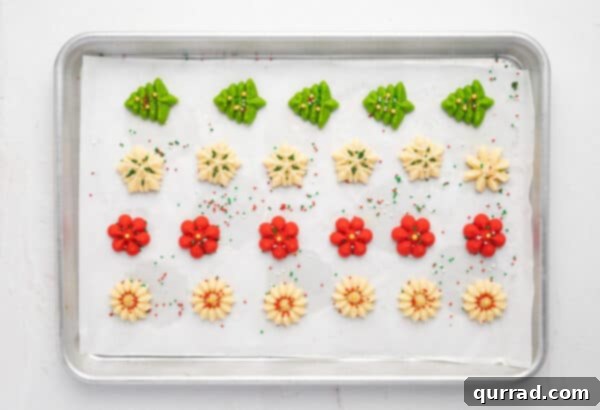 Pressed spritz cookie dough arranged on a parchment-lined baking sheet, topped with colorful sprinkles before baking.
