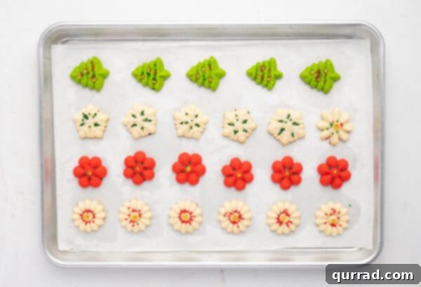 Freshly baked spritz cookies cooling on a parchment-lined baking sheet, showing their slightly golden edges.