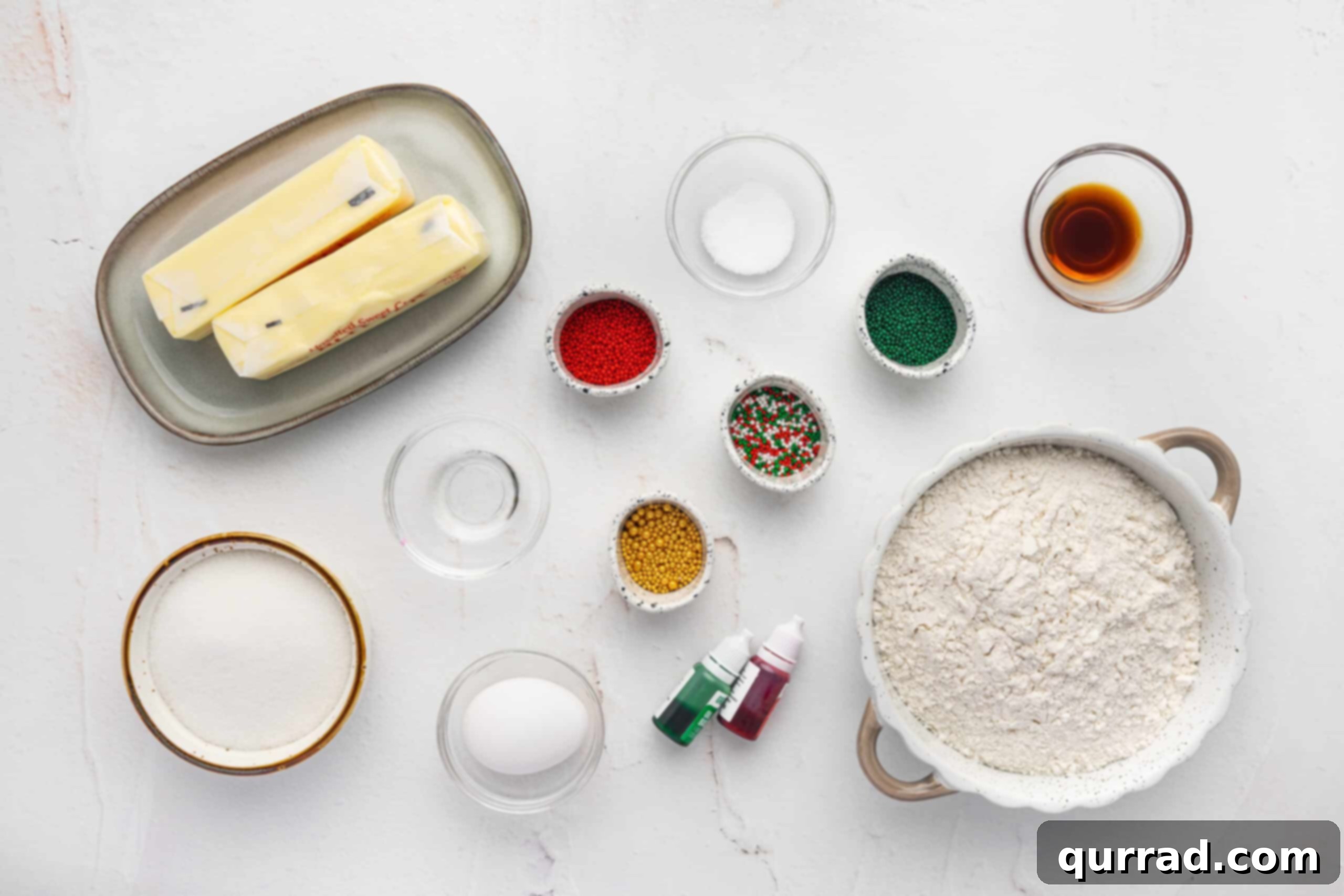 Pressed Butter Cookies 3 A collection of spritz cookie ingredients laid out on a clean surface, including butter, sugar, flour, extracts, and colorful sprinkles.