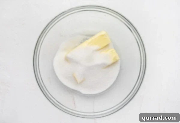 Granulated sugar and two sticks of butter in a glass mixing bowl, being creamed together with a hand mixer.