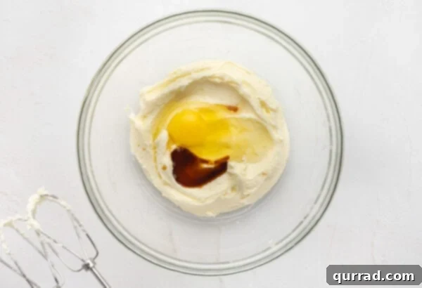 Vanilla extract and eggs added to creamed butter and sugar mixture in a glass mixing bowl, ready for blending.