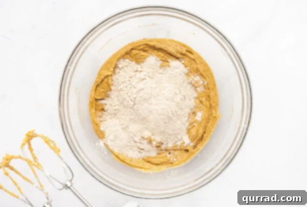 Flour gradually added to the wet ingredients for gingerbread cookies in a glass mixing bowl, starting to form a dough.