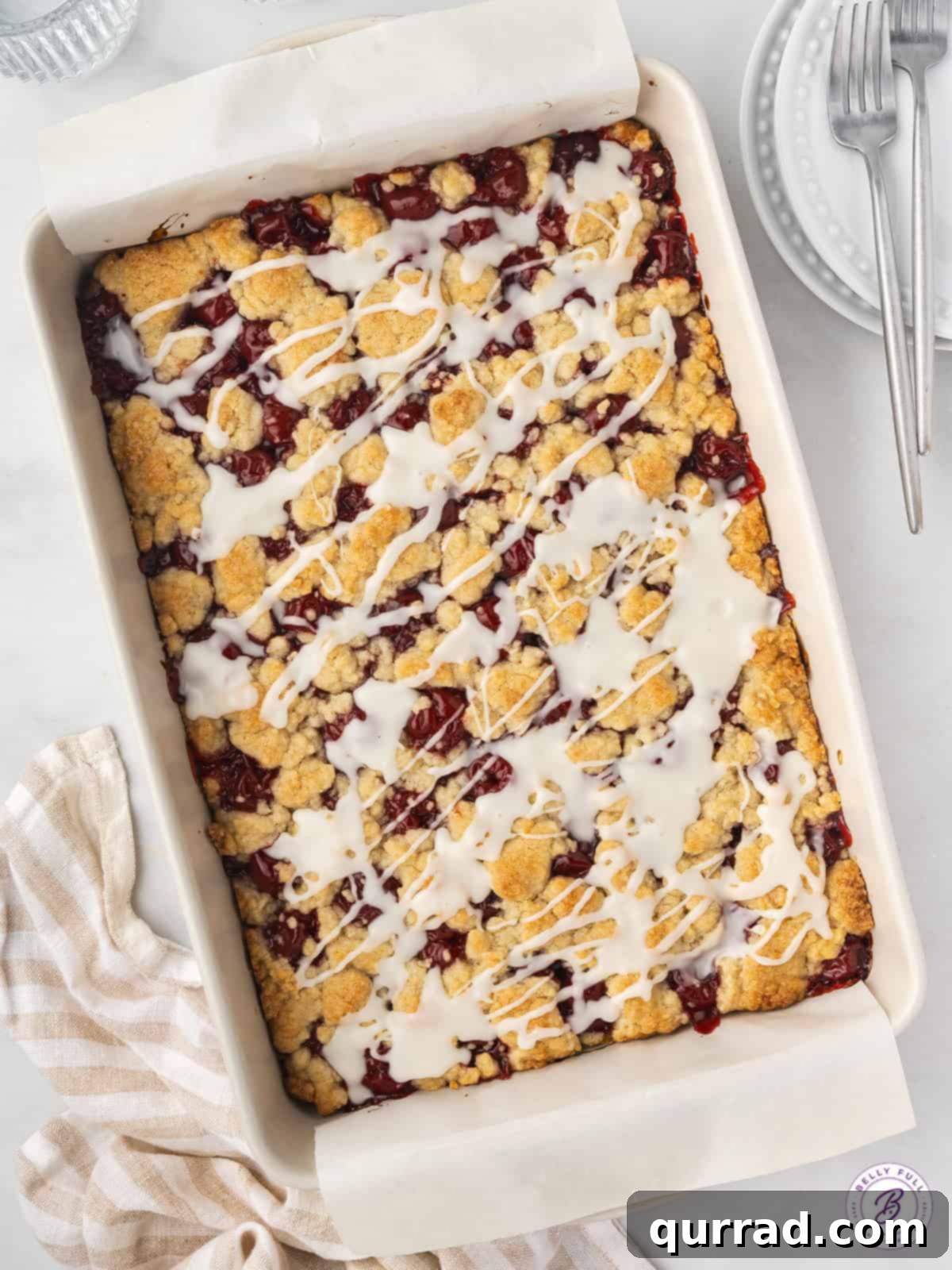 Freshly baked Cherry Pie Bars with bubbly filling and golden crumble, cooling in the pan. An inviting overhead view of a 9x13 baking dish filled with freshly baked cherry pie bars, topped with a delicate glaze, ready for slicing.