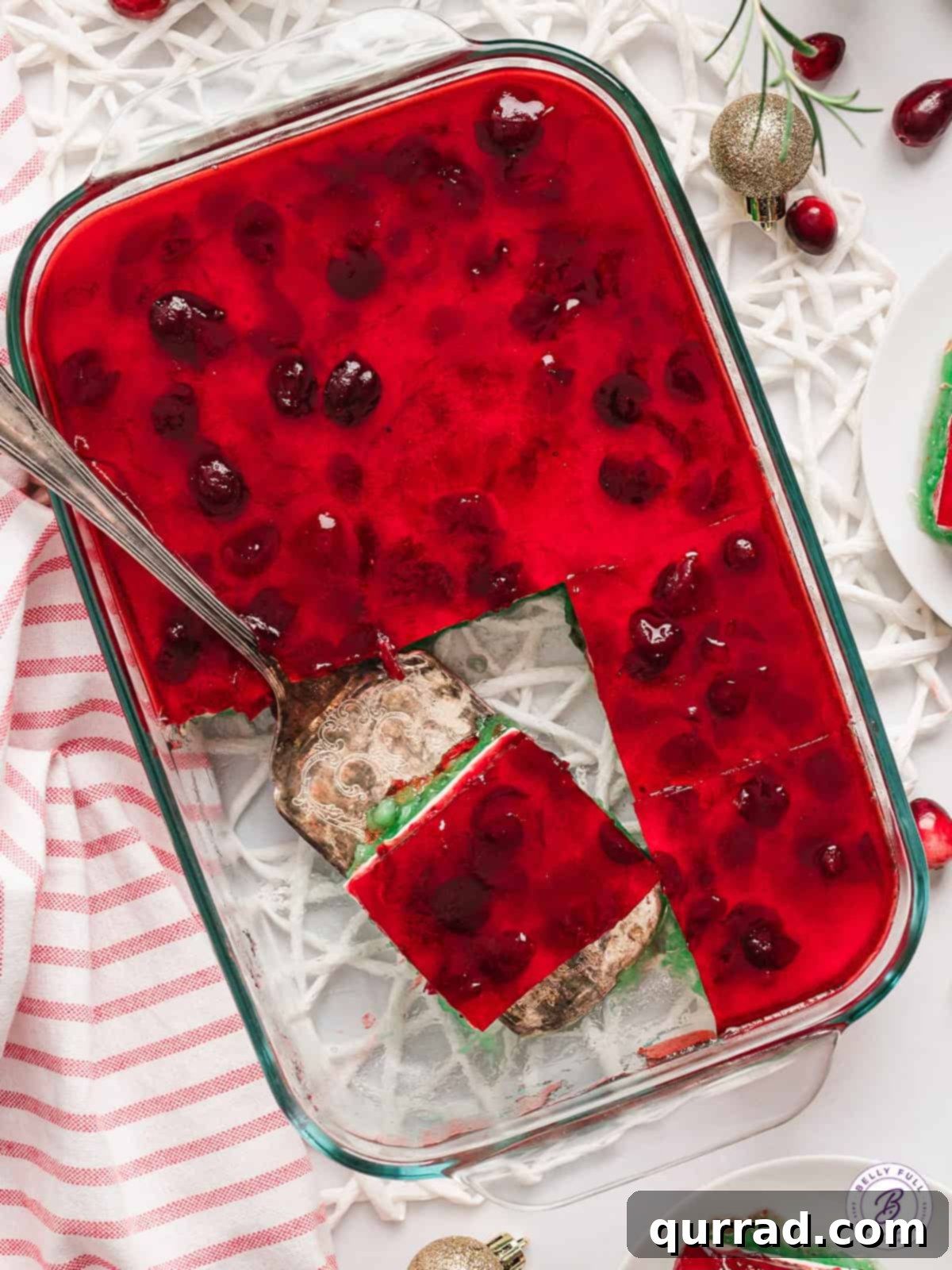 Easy Layered Christmas Jello Ready for Serving An overhead view of a glass baking dish filled with beautifully layered Christmas jello, with one perfect slice being lifted out by a serving spatula.