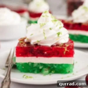 A slice of layered Christmas jello topped with whipped cream on a plate