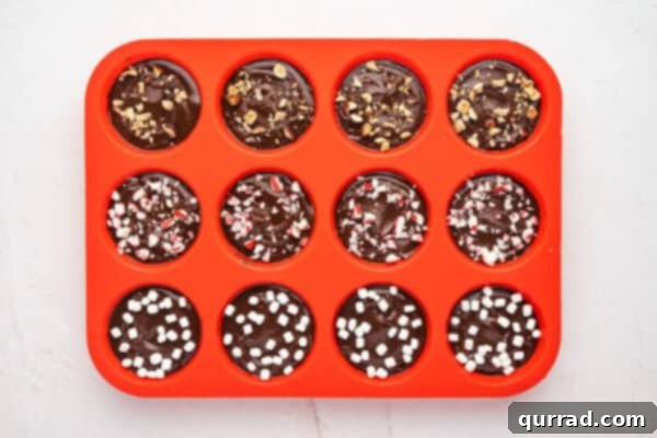 Melted chocolate in a silicone muffin tin topped with marshmallow bits, crushed nuts, and crushed peppermint.