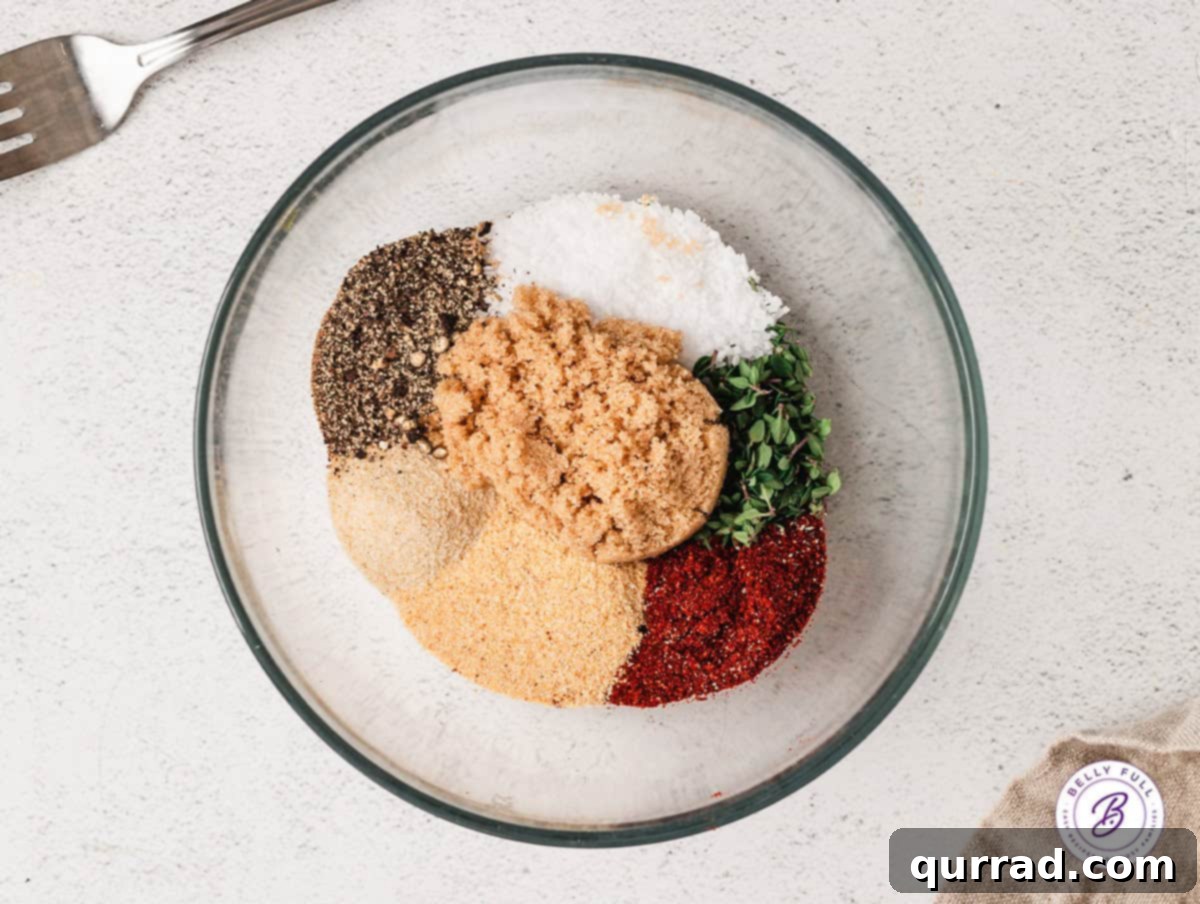 An overhead shot showcasing all the essential ingredients for the prime rib rub: sea salt, black pepper, fresh rosemary, fresh thyme, onion powder, smoked paprika, and dark brown sugar, beautifully arranged in a glass mixing bowl.